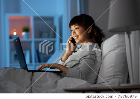 woman with laptop calling on phone in bed at night woman with laptop calling on phone in bed at night 78766979