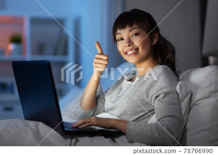 woman with laptop in bed at night shows thumbs up 78766990