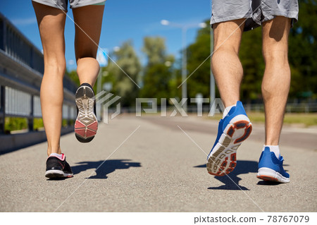 feet of sporty couple running along city road 78767079