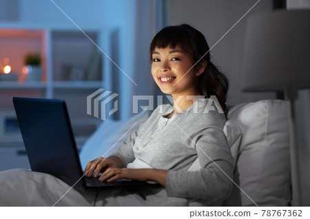 woman with laptop in bed at home at night woman with laptop in bed at home at night 78767362