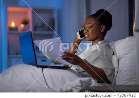 woman with laptop calling on smartphone in bed woman with laptop calling on smartphone in bed 78767418