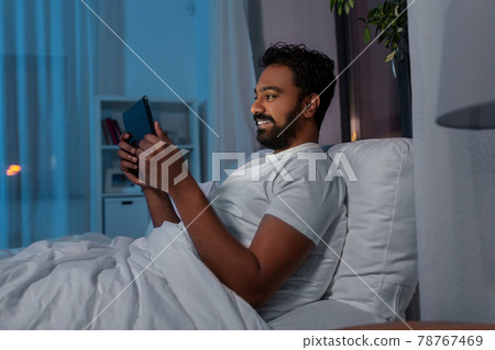 indian man with tablet pc in bed at home at night 78767469
