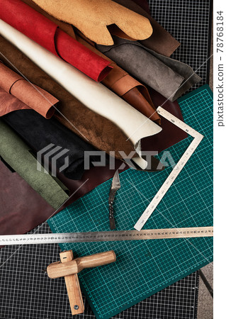 Samples of genuine leather of different colors are rolled up on a table with mats and tools for cutting pieces of leather, a workshop for sewing leather goods Samples of genuine leather of different colors are rolled up on a table with mats and tools for cutting pieces of leather, a workshop for sewing leather goods 78768184