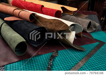 Rolled up samples of textures of genuine leather of different colors on a leather background, on a table with mats and tools for cutting pieces of leather 78768186