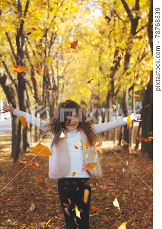 Beautiful little girl throwing fallen leaves, playing in the park; autumn/nature background 78768839