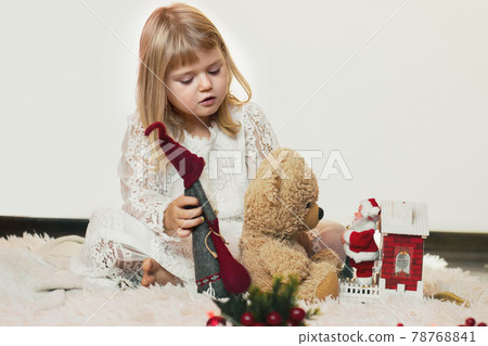 Cute little blond girl sitting on the floor, playing with her teddy bear and little Santa Claus Christmas toy 78768841