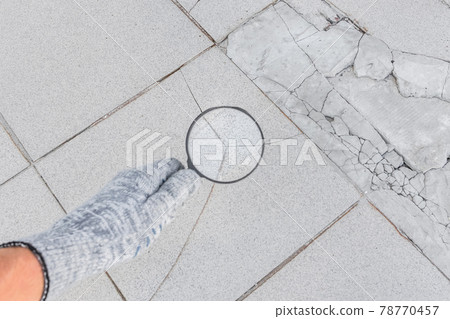 The hand of an industrial worker in a construction glove with a magnifying glass examines the damaged cracked tile background. Renovation concept The hand of an industrial worker in a construction glove with a magnifying glass examines the damaged cracked tile background. Renovation concept 78770457