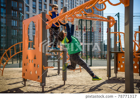 Active little child playing climbing spring metal at school yard playground. Kids play and climb outdoors under sunset, shallow Focus. 78771317
