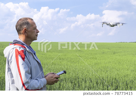 aerial photography of agricultural crops . a man with a quadrocopter on the background of a field and a blue sky aerial photography of agricultural crops . a man with a quadrocopter on the background of a field and a blue sky 78773415