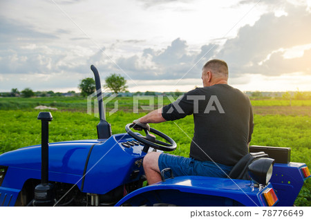 Farmer drives a tractor. Harvesting crops campaign, earthworks. Agroindustry and agribusiness. Countryside farmland. Farming. Agricultural machinery management. Farmer drives a tractor. Harvesting crops campaign, earthworks. Agroindustry and agribusiness. Countryside farmland. Farming. Agricultural machinery management. 78776649