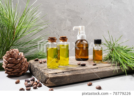 Composition of set of small glass bottles of essential cedar oil on old wooden board with cedar branches, cone and nuts on grey. Herbal medicine, spa coniferous concept. Copy space. Horizontal photo. Composition of set of small glass bottles of essential cedar oil on old wooden board with cedar branches, cone and nuts on grey. Herbal medicine, spa coniferous concept. Copy space. Horizontal photo. 78779226