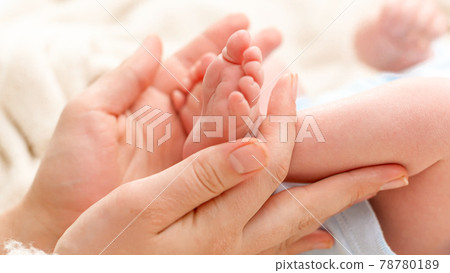 Closeup of woman gently stroking with hand tiny feet of her newborn baby son with perfect skin. Concept of family happiness and loving parents with little children Closeup of woman gently stroking with hand tiny feet of her newborn baby son with perfect skin. Concept of family happiness and loving parents with little children 78780189