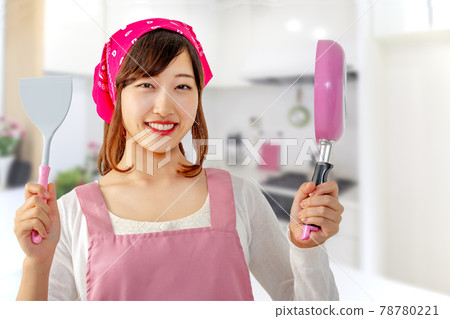 A smiling young woman holding a frying pan and a frying pan in the kitchen 78780221
