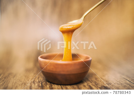 Manuka honey spoon dipped in golden liquid natural superfood on wooden background 78780343