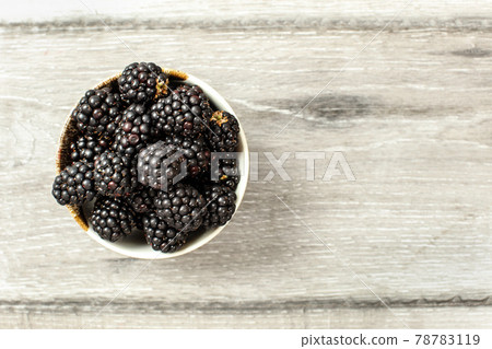 Tabletop view, small ceramic cup with blackberries on gray wood desk. Space for text on the right. Tabletop view, small ceramic cup with blackberries on gray wood desk. Space for text on the right. 78783119