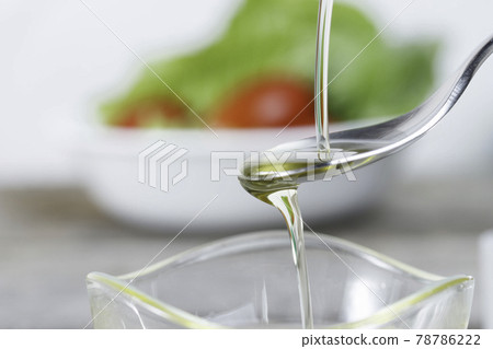 Olive oil dripping in a bowl against the background of salad 78786222