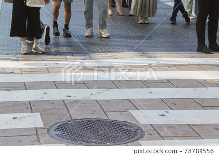 At the feet of people waiting for the pedestrian crossing 78789556