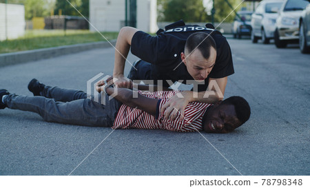 Angry police officer interrogating African American guy on ground 78798348