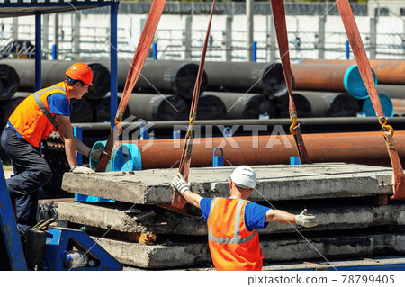 Two slingers unload concrete slabs on the street on a summer day. Workers in construction helmets 78799405