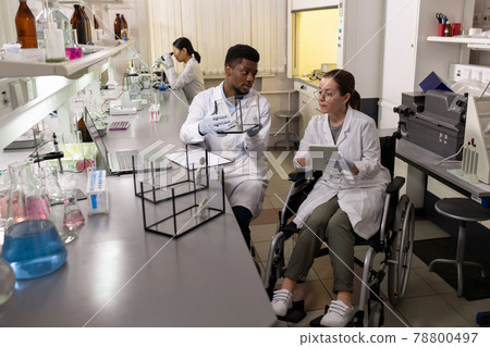 Woman in wheelchair using tablet and looking at mouse in glass box held by African male colleague 78800497