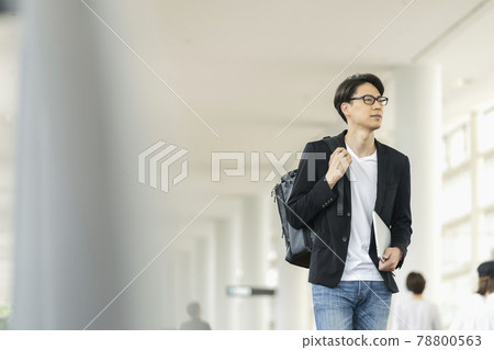 A man in his thirties walking with his laptop and backpack A man in his thirties walking with his laptop and backpack 78800563
