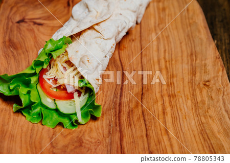 pita tortilla roll with vegetables and cheese on a wooden cutting board.  78805343
