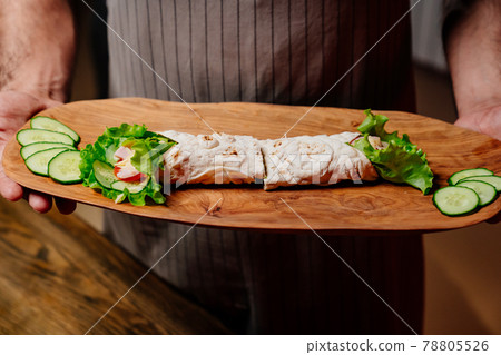 pita with vegetables and chopped cucumbers on a cutting board in the hands 78805526