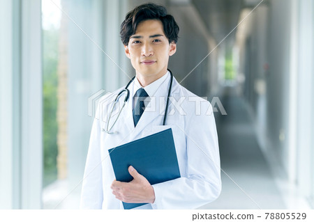A young male doctor in a lab coat standing in the hospital corridor A young male doctor in a lab coat standing in the hospital corridor 78805529