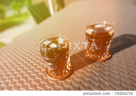 Two glasses with a cocktail of whiskey with ice on the summer table on the street. Two glasses with a cocktail of whiskey with ice on the summer table on the street. 78808258