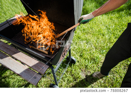 A man in gloves straightens burning wood in the grill. Summer barbecue. A man in gloves straightens burning wood in the grill. Summer barbecue. 78808267
