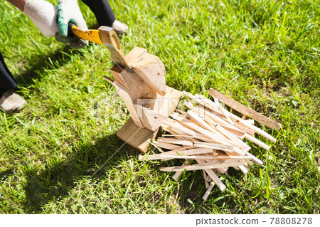 A man in gloves chopping wood with an ax on the green grass in summer. A man in gloves chopping wood with an ax on the green grass in summer. 78808278
