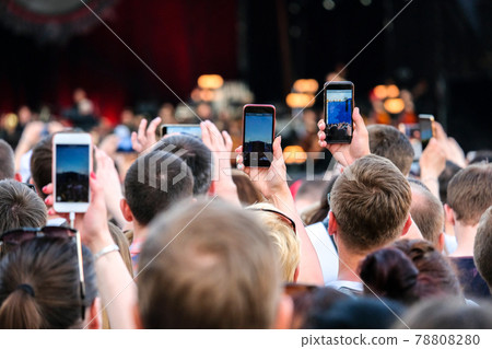 Raised outstretched hands with smartphones photographing stage in the crowd during a concert. Raised outstretched hands with smartphones photographing stage in the crowd during a concert. 78808280