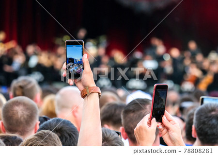Raised outstretched hand with smartphone photographing stage in the crowd during a concert. Raised outstretched hand with smartphone photographing stage in the crowd during a concert. 78808281
