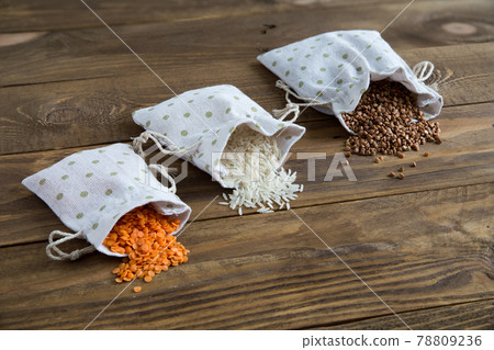 Three types of cereals buckwheat, rice and lentils in canvas bags. They lie on wooden background. Grains are scattered on table. Organic healthy cereals. Natural vegetarian vegetable protein. Close up Three types of cereals buckwheat, rice and lentils in canvas bags. They lie on wooden background. Grains are scattered on table. Organic healthy cereals. Natural vegetarian vegetable protein. Close up 78809236