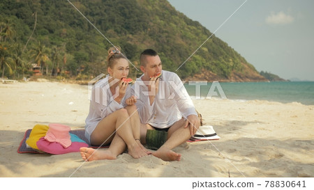 The cheerful love couple holding and eating slices of watermelon on tropical sand beach sea. Romantic lovers two people spend summer weekend. 78830641