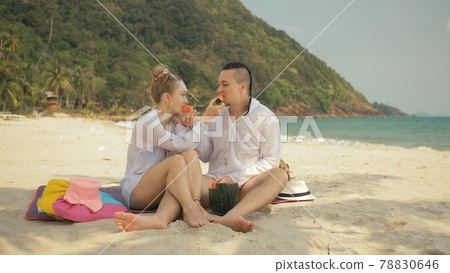 The cheerful love couple holding and eating slices of watermelon on tropical sand beach sea. Romantic lovers two people spend summer weekend. 78830646