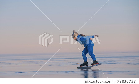 The child train on ice professional speed skating. The girl skates in the winter in sportswear, sport glasses, suit. Outdoor slow motion. 78830738