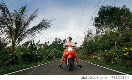 Scooter road trip. Love couple on red motorbike in white clothes on forest road trail. Just married woman and man kiss, hugs, sit on motorbike. Scooter road trip. Love couple on red motorbike in white clothes on forest road trail. Just married woman and man kiss, hugs, sit on motorbike. 78831394