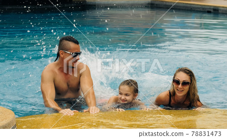 The mother and father with little daughter have fun in the pool. Mom and dad plays with the child. The family enjoy summer vacation in a swimming. 78831473