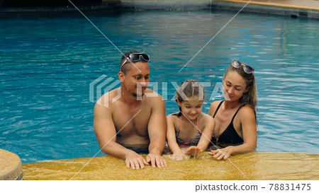 The mother and father with little daughter have fun in the pool. Mom and dad plays with the child. The family enjoy summer vacation in a swimming. The mother and father with little daughter have fun in the pool. Mom and dad plays with the child. The family enjoy summer vacation in a swimming. 78831475