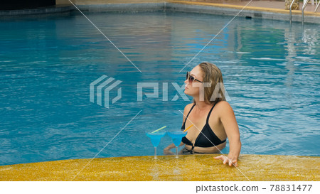 The wide middle shot pretty woman drinking blue cocktail alcohol liquor in swimming pool at hotel. Portrait of sexy girl in pool outdoor. 78831477