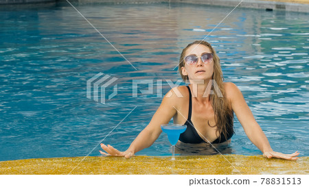 The wide middle shot pretty woman drinking blue cocktail alcohol liquor in swimming pool at hotel. Portrait of sexy girl in pool outdoor. The wide middle shot pretty woman drinking blue cocktail alcohol liquor in swimming pool at hotel. Portrait of sexy girl in pool outdoor. 78831513