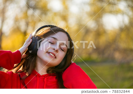 Happy girl listening to music with headphones in park. Teenage girl in wireless headphones. Happy girl listening to music with headphones in park. Teenage girl in wireless headphones. 78832844