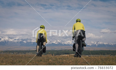 The man and woman travel on mixed terrain cycle touring with bikepacking. The two people journey with bicycle bags. Mountain snow capped. The man and woman travel on mixed terrain cycle touring with bikepacking. The two people journey with bicycle bags. Mountain snow capped. 78833072