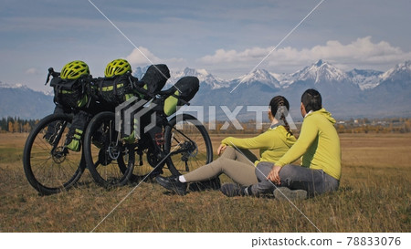 The man and woman travel on mixed terrain cycle touring with bikepacking. The two people journey with bicycle bags. Mountain snow capped. The man and woman travel on mixed terrain cycle touring with bikepacking. The two people journey with bicycle bags. Mountain snow capped. 78833076