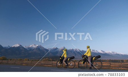 The man and woman travel on mixed terrain cycle touring with bikepacking. The couple journey with bicycle bags. Mountain snow capped. The man and woman travel on mixed terrain cycle touring with bikepacking. The couple journey with bicycle bags. Mountain snow capped. 78833103