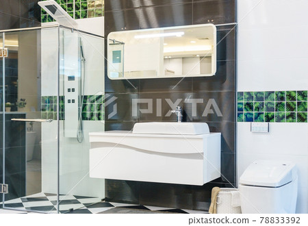 Spacious and bright modern bathroom interior with white walls, a shower cabin with glass wall, a toilet and faucet sink Spacious and bright modern bathroom interior with white walls, a shower cabin with glass wall, a toilet and faucet sink 78833392