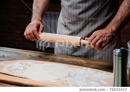 hands roll the dough into a thin layer. Cooking pizza, noodles or pitta at home hands roll the dough into a thin layer. Cooking pizza, noodles or pitta at home 78833423