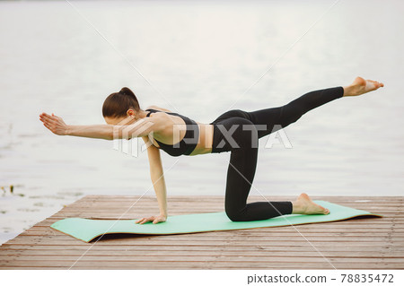 Woman practicing advanced yoga by the water Woman practicing advanced yoga by the water 78835472