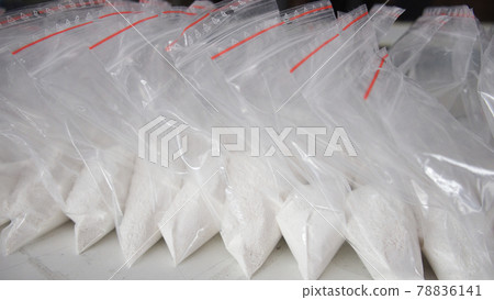 A large number of transparent sachets filled with white powder. White powder packaged in small sachets. A large number of transparent sachets filled with white powder. White powder packaged in small sachets. 78836141